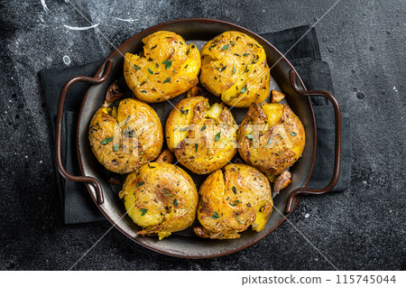 Broken potatoes baked in oil with herbs. Black background. Top view 115745044