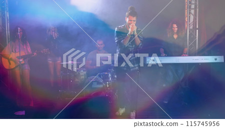 Image of glowing blue lights over caucasian man singing with band playing on stage Image of glowing blue lights over caucasian man singing with band playing on stage 115745956