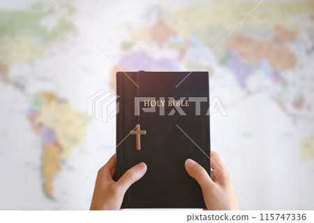 Christian holding the holy cross of Jesus Christ and the Bible in his hands and praying for missions, gospel and evangelism, world map background Christian holding the holy cross of Jesus Christ and the Bible in his hands and praying for missions, gospel and evangelism, world map background 115747336