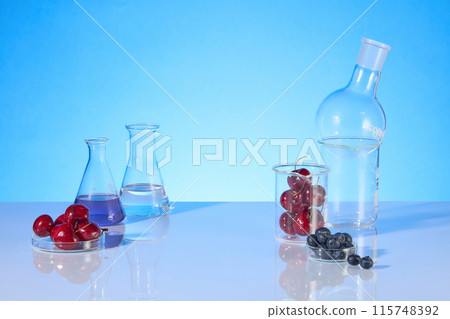 Template for designing over blue background from front view, on both sides decorated with experiment utensils, which contain ripe cherry, blueberry and extract from it. Blank space for designing 115748392