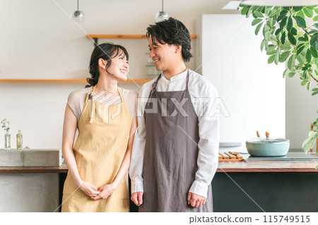 A couple, lover, or partner wearing an apron laughing in the kitchen or dining room of their home A couple, lover, or partner wearing an apron laughing in the kitchen or dining room of their home 115749515