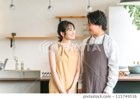 A couple, lover, or partner wearing an apron laughing in the kitchen or dining room of their home A couple, lover, or partner wearing an apron laughing in the kitchen or dining room of their home 115749516