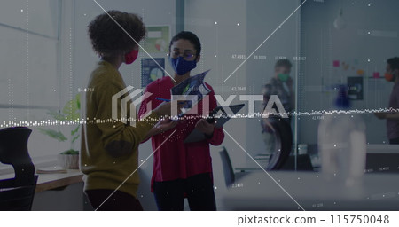 Data processing over two diverse female office colleagues wearing face masks discussing at office 115750048