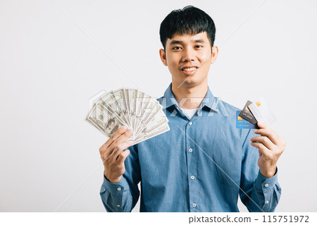 A confident Asian man smiles while holding dollars and a credit card for payment in his hand. Studio shot isolated on white background, showcasing financial success. 115751972