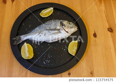 Raw fresh fish dorado with lemon and spices on wooden table. Top view Raw fresh fish dorado with lemon and spices on wooden table. Top view 115754575