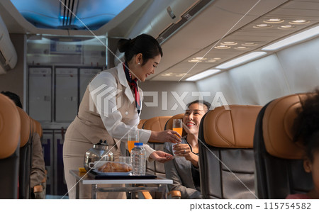 Airplane flight attendant serving orange juice to female passenger in cabin. 115754582