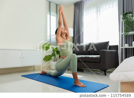 Happiness woman in green top and leggings doing yoga in Low Lunge pose or Anjaneyasana on blue mat in bedroom at home.. Happiness woman in green top and leggings doing yoga in Low Lunge pose or Anjaneyasana on blue mat in bedroom at home.. 115754589