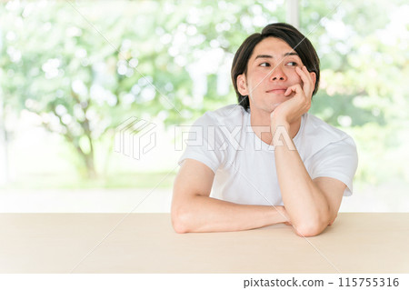 一位身穿白色 T 卹、清新綠色背景的亞洲年輕男子(思考與擔憂) 一位身穿白色 T 卹、清新綠色背景的亞洲年輕男子(思考與擔憂) 115755316