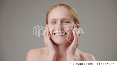 Real people - age, beauty, health and dry skin care concept - beautiful mature Caucasian middle aged woman in her 50s touching facial skin with bright toothy smile and good mood 115756027