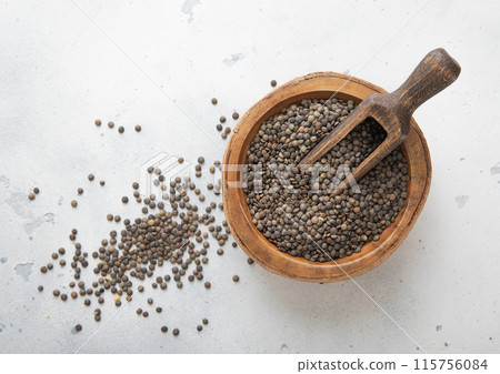 Raw dry black lentils seeds in wooden bowl with scoop on light table. 115756084
