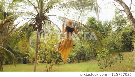 Tropical Escape: Woman in Yellow Dress Swinging Under Palm Trees 115757025