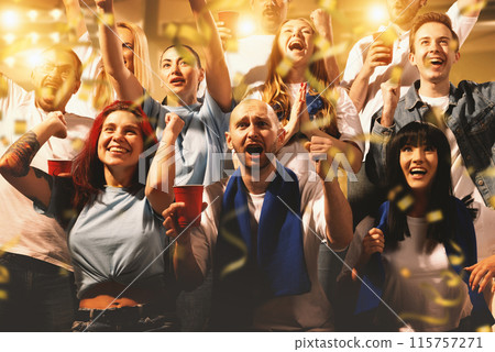 Crowd of sport fans cheering during match on stadium. Excited people standing raised arms , clapping and yelling to encourage their team Crowd of sport fans cheering during match on stadium. Excited people standing raised arms , clapping and yelling to encourage their team 115757271