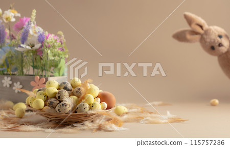 Easter eggs, feathers, spring flowers, and toy bunny on a beige background. 115757286