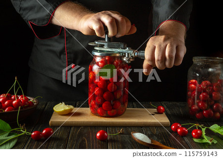 A chef rolls up a jar of ripe cherries for canning with a hand seaming key. Cooking or canning cherry compote in the kitchen 115759143