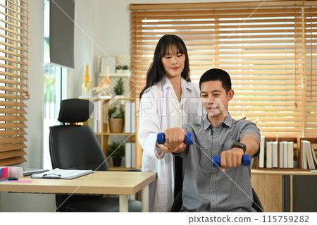 Female physical therapist guiding male patient in weight training exercise at clinic 115759282