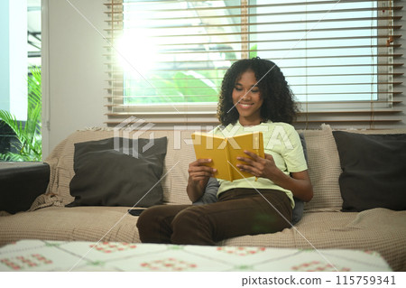 Relaxed African American woman reading a book, sitting on sofa in living room Relaxed African American woman reading a book, sitting on sofa in living room 115759341