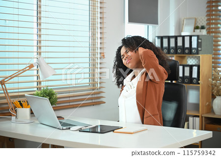 Overworked African American businesswoman massaging her neck to relieve pain in muscles after long hours work 115759342