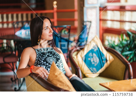 A beautiful woman in an Oriental dress is sitting on a sofa with pillows. The concept of luxury living 115759738
