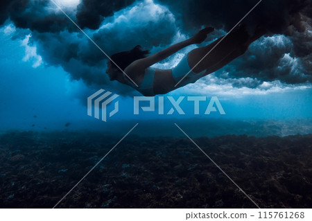 Woman swims under breaking wave with foam in blue ocean. Extreme duck dive under crashing waves Woman swims under breaking wave with foam in blue ocean. Extreme duck dive under crashing waves 115761268