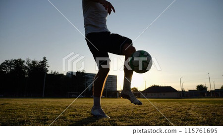 Legs of young man kicking ball at green field. Male feet of professional footballer juggling soccer ball on stadium at sunset. Sportsman practicing tricks outdoor. Concept of a freestyle football Legs of young man kicking ball at green field. Male feet of professional footballer juggling soccer ball on stadium at sunset. Sportsman practicing tricks outdoor. Concept of a freestyle football 115761695