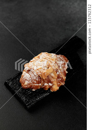 Almond croissant. puff pastry, delicate frangipane cream with almonds, enriched with butter. On top, the croissant has a hint of almond flakes and powdered sugar. on a black cutting board Almond croissant. puff pastry, delicate frangipane cream with almonds, enriched with butter. On top, the croissant has a hint of almond flakes and powdered sugar. on a black cutting board 115762312