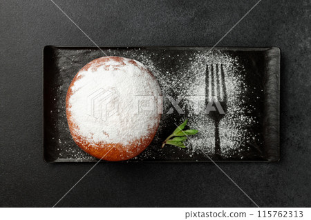 An appetizing donut with strawberries sprinkled with powdered sugar on a black rectangular plate on a gray background An appetizing donut with strawberries sprinkled with powdered sugar on a black rectangular plate on a gray background 115762313