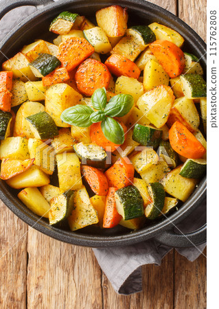 Seasonal fried vegetables such as potatoes, carrots, zucchini close-up in a frying pan on the table. Vertical top view Seasonal fried vegetables such as potatoes, carrots, zucchini close-up in a frying pan on the table. Vertical top view 115762808