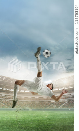 Vertical image of determined man, soccer player in white uniform hitting ball in jump and falling down, scoring goal. 3D render of stadium 115763194