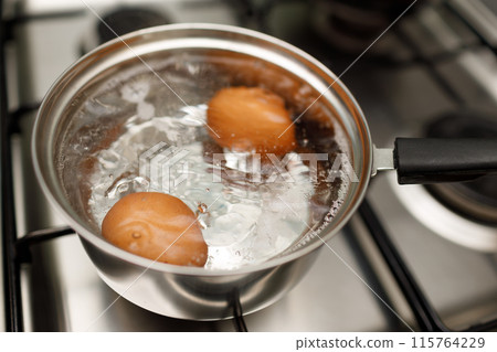Saucepan stainless steel with boiling eggs breakfast in a water on a gas stove. 115764229