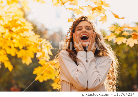 Smiling young amaxed woman enjoy the autumn weather in the parkland with the yellow leaves at branches 115764234