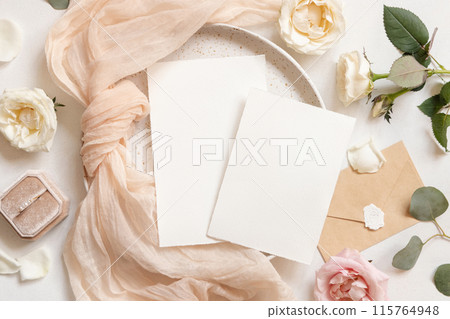 Cards near roses, cream fabric and ring on plates top view, copy space, wedding mockup 115764948