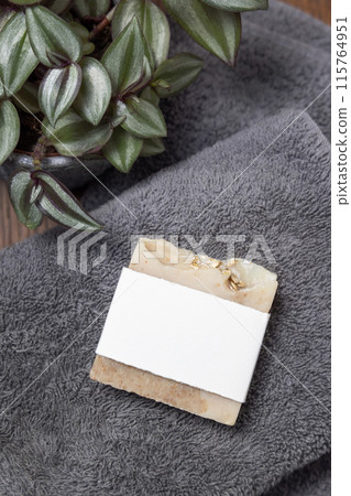 Soap bar with blank label on grey folded towel near green plant on wood in bathroom, mockup Soap bar with blank label on grey folded towel near green plant on wood in bathroom, mockup 115764951