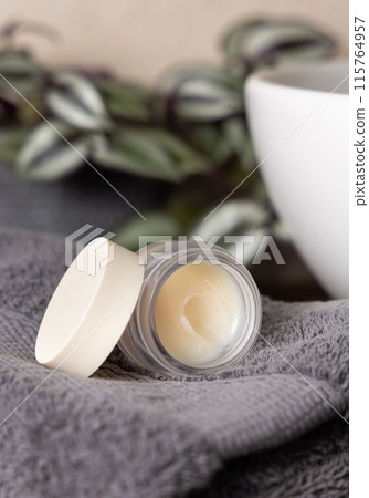 Opened lip balm jar on dark grey towels, near plant and basin on wood in bathroom, mockup Opened lip balm jar on dark grey towels, near plant and basin on wood in bathroom, mockup 115764957