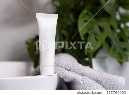 White cream squeeze tube on vessel sink near grey towels and plant close up, cosmetic mockup White cream squeeze tube on vessel sink near grey towels and plant close up, cosmetic mockup 115764963
