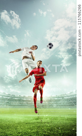 Dynamic, vertically-oriented photo. Soccer players in red and white jerseys in mid-air, competing for ball in stadium filled with cheering spectators. Dynamic, vertically-oriented photo. Soccer players in red and white jerseys in mid-air, competing for ball in stadium filled with cheering spectators. 115766266