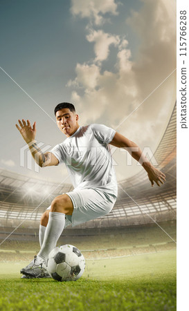 Vertical orientation. Focused on game soccer player in white attire deftly maneuvers ball on field, highlighted by bright stadium lights. 115766288