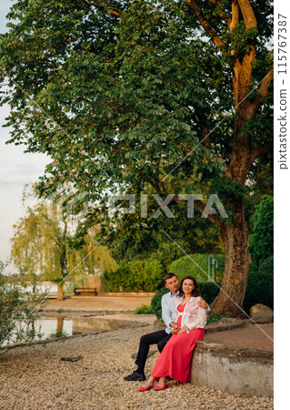 man and pregnant woman in red dress at sunset on the riverbank man and pregnant woman in red dress at sunset on the riverbank 115767387