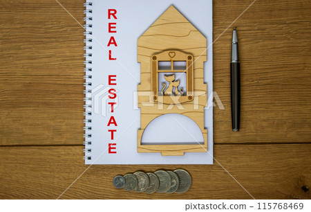 White note with inscription 'real estate' on beautiful wooden table, metalic pen, coins and miniature wooden house. Business concept. 115768469