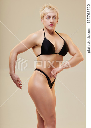 Medium full shot of attractive lady bodybuilder showing off chest and arm muscles isolated in studio on neutral background Medium full shot of attractive lady bodybuilder showing off chest and arm muscles isolated in studio on neutral background 115768720