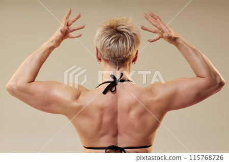 Rear view of unrecognizable lady bodybuilder in back double biceps pose demonstrating broad shoulders and muscular arms isolated in studio on neutral background Rear view of unrecognizable lady bodybuilder in back double biceps pose demonstrating broad shoulders and muscular arms isolated in studio on neutral background 115768726