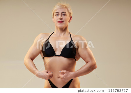 Medium shot of sportswoman with solid muscles performing front lat spread pose highlighting back and shoulder width, overall torso silhouette isolated in studio on neutral background, copy space 115768727