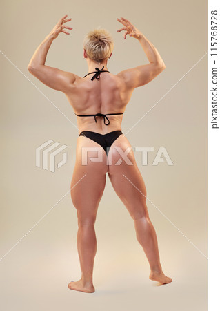 Vertical shot of athletic female model in back double biceps pose showing back size and symmetry in tandem with arms, shoulders, hamstrings and calf isolated in studio on neutral background 115768728