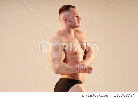 Side view of strong bodybuilder topless with hard arm muscles giving side chest pose. Athletic sportsman demonstrating pumped up biceps on neutral background, copy space Side view of strong bodybuilder topless with hard arm muscles giving side chest pose. Athletic sportsman demonstrating pumped up biceps on neutral background, copy space 115768754