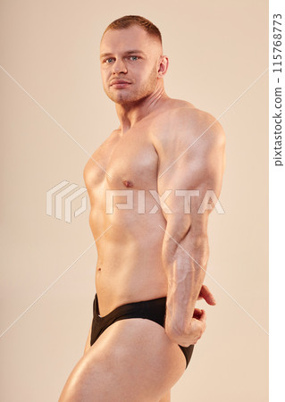 Medium long shot portrait of confident bodybuilder performing side triceps pose topless. Handsome sportsman showing arm and chest muscles looking at camera isolated on neutral background Medium long shot portrait of confident bodybuilder performing side triceps pose topless. Handsome sportsman showing arm and chest muscles looking at camera isolated on neutral background 115768773