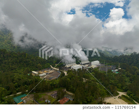 Aerial view of Geothermal station with steam and pipes. Geothermal power plant with smoking pipes and steam. Mindanao, Philippines. Aerial view of Geothermal station with steam and pipes. Geothermal power plant with smoking pipes and steam. Mindanao, Philippines. 115769154
