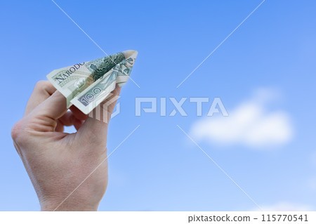 Hand holding the plane made of 100 polish zloty on a blue sky with clouds background. Hand holding the plane made of 100 polish zloty on a blue sky with clouds background. 115770541