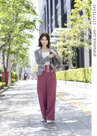 A businesswoman in her 30s smiling at the camera, office district, full body 115771343