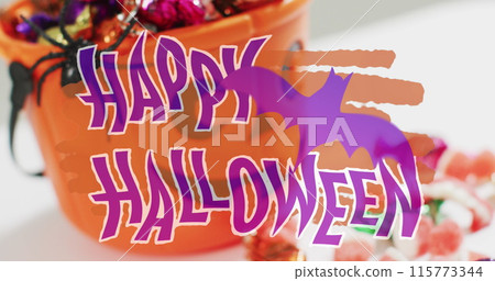 Happy halloween text banner with bat icon against pumpkin shaped bucket full of halloween candies 115773344
