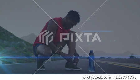 Image of blue light trails against african american fit man tying shoe laces on the road 115774753