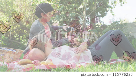 Image of heart emojis over happy caucasian female couple in love drinking wine 115776283